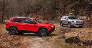Forest scene with the 2019 silver Jeep Cherokee Latitude and red Cherokee Trailhawk.